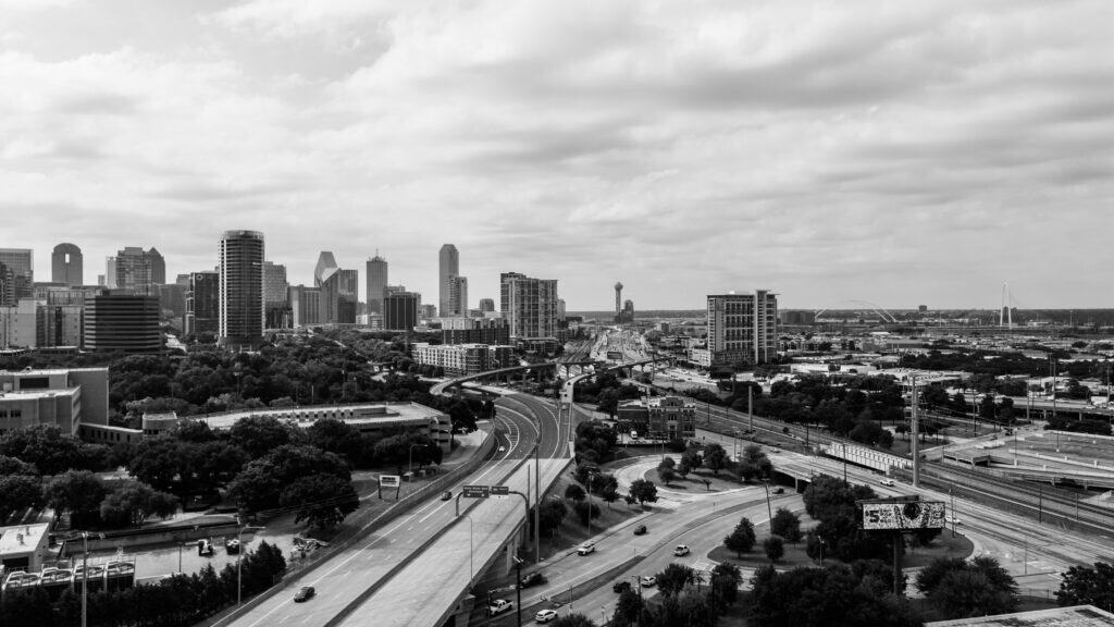 Black-and-white view of Dallas, Texas skyline with highways, overpasses, and the Margaret Hunt Hill Bridge, representing logistics, transportation, and supply chain infrastructure.
