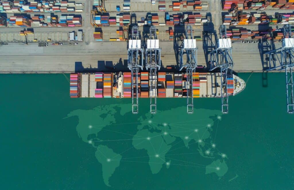 Aerial view of global shipping port with cargo containers, container ship, and worldwide supply chain logistics network overlay.